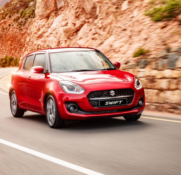Red Suzuki Swift driving on winding open road at sunset
