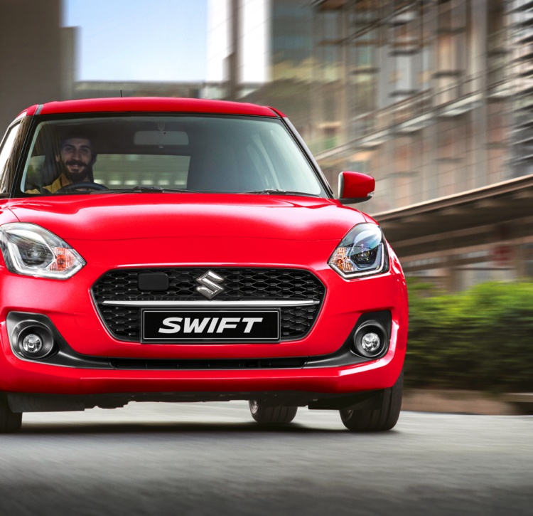 Vibrant Suzuki Swift hatchback cruises city streets with smiling driver
