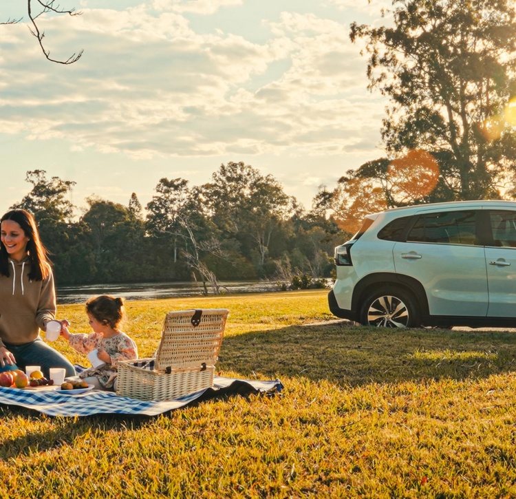 Family enjoys a picnic by the river with Suzuki S-CROSS parked nearby