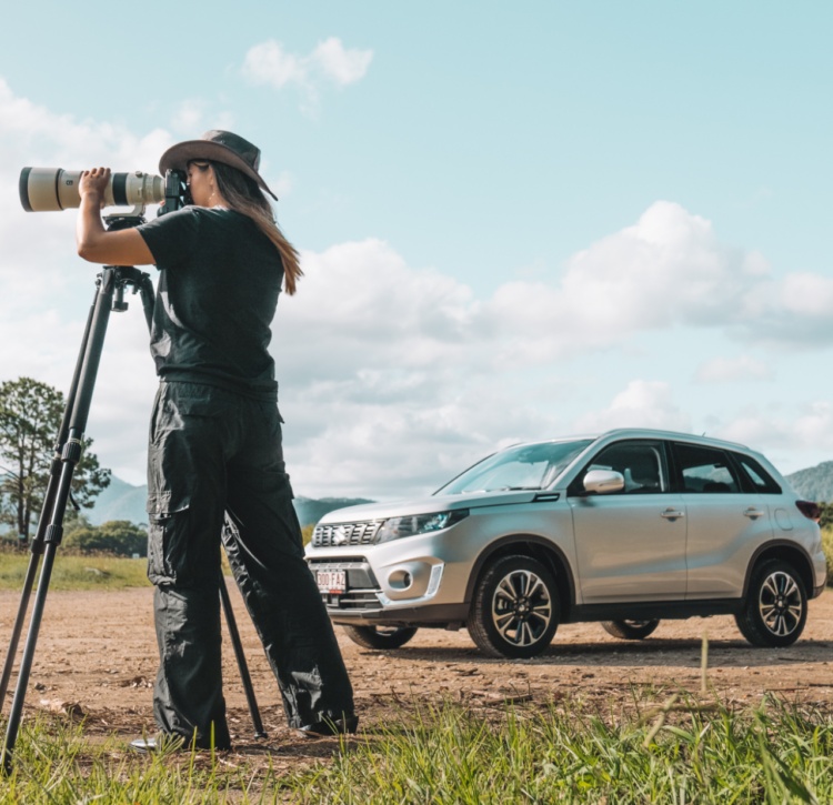 Photographer with camera and tripod takes a photo in a crop field with Suzuki Vitara