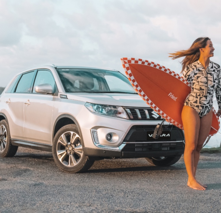 Female with surfboard in front of Vitara
